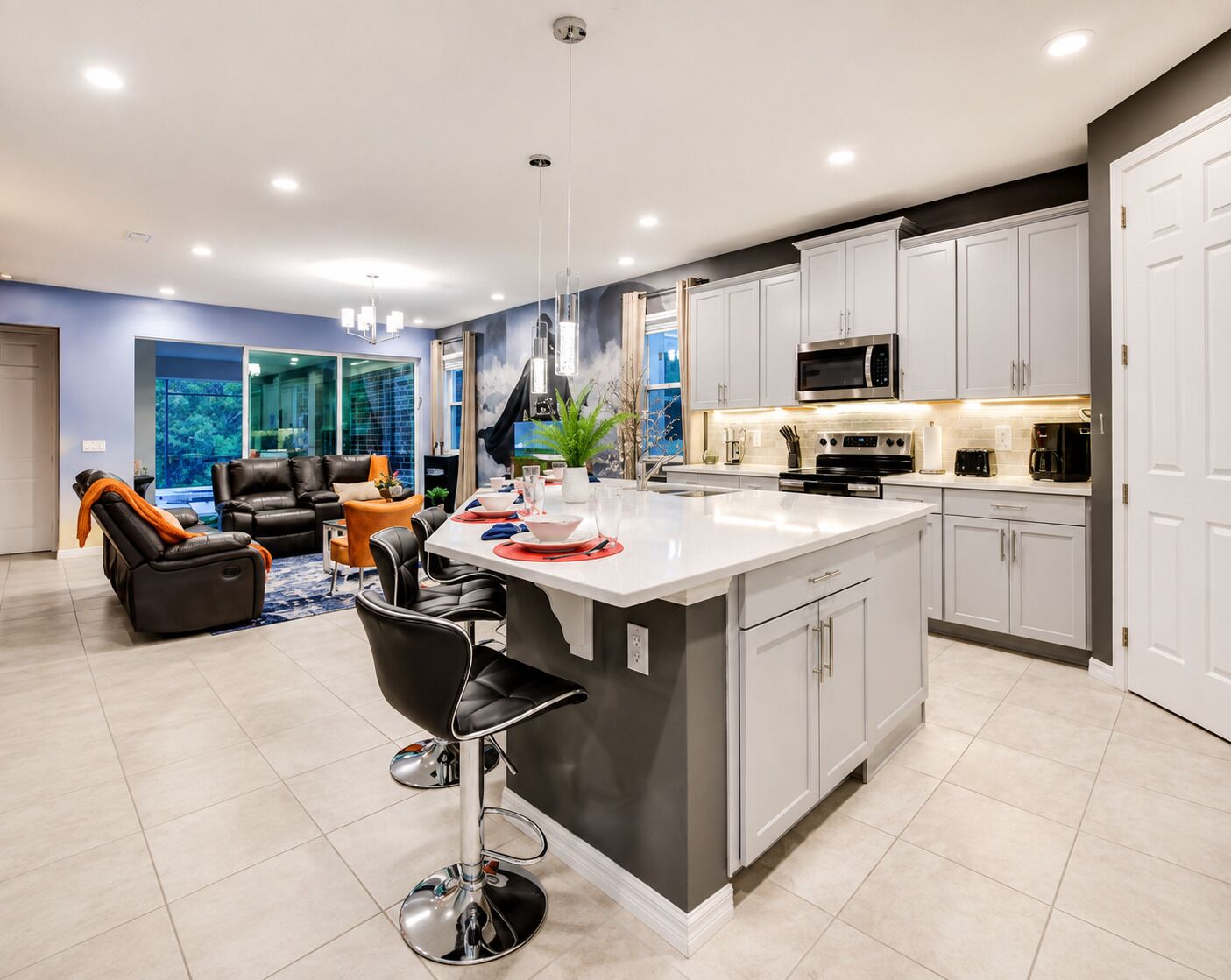 A modern kitchen with white cabinets, a central island, and a dining area with a black leather sofa and a bar stool.