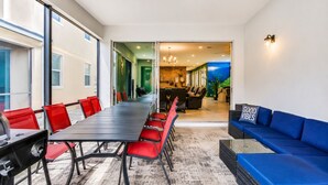 Un salón de conferencias con una larga mesa y sillas rojas, un sofá azul y vistas hacia una zona de cocina.
