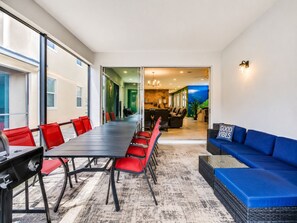 A conference room with a long table and red chairs, a blue sofa, and a view into a kitchen area. - Suncrest Residence (Kissimmee)