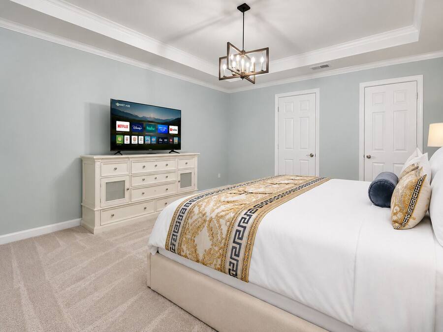 Quarto com cama, televisão sobre um penteadeira e ventilador de teto.