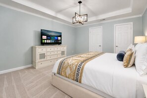 A bedroom with a bed, a TV on a dresser, and a ceiling fan. - Suncrest Residence (Kissimmee)