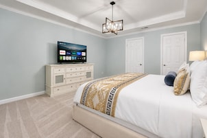 Quarto com cama, televisão sobre um penteadeira e ventilador de teto.