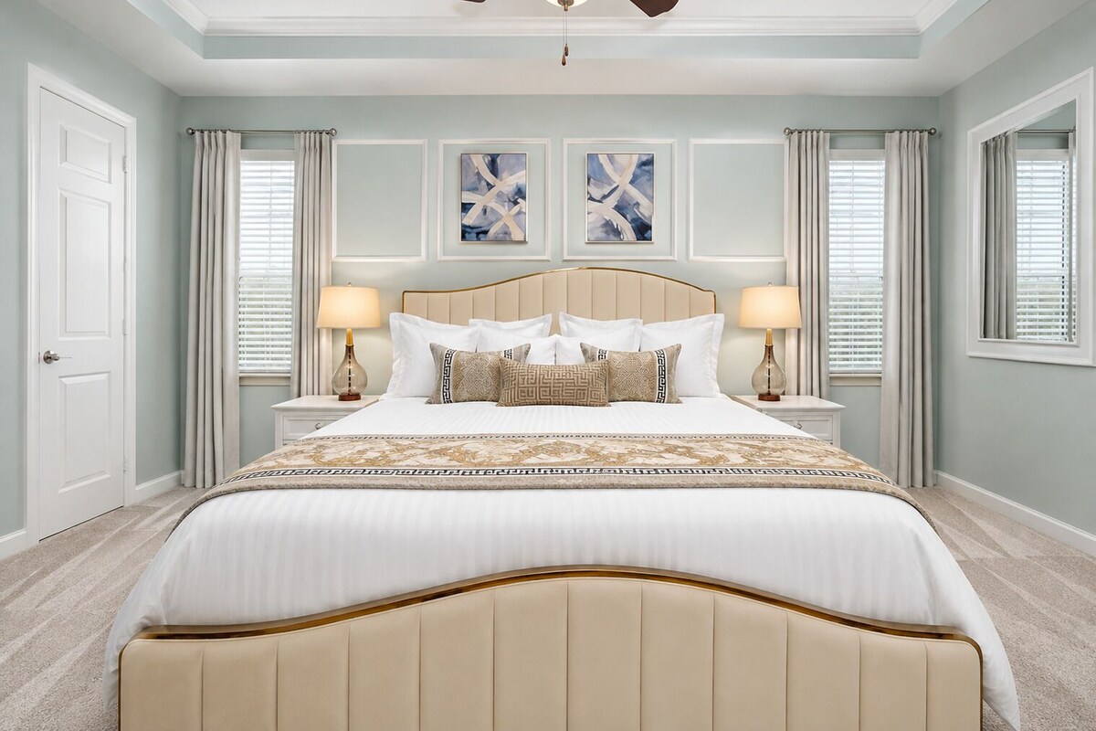 A bedroom with a large bed, two bedside tables, a ceiling fan, and artwork on the walls.