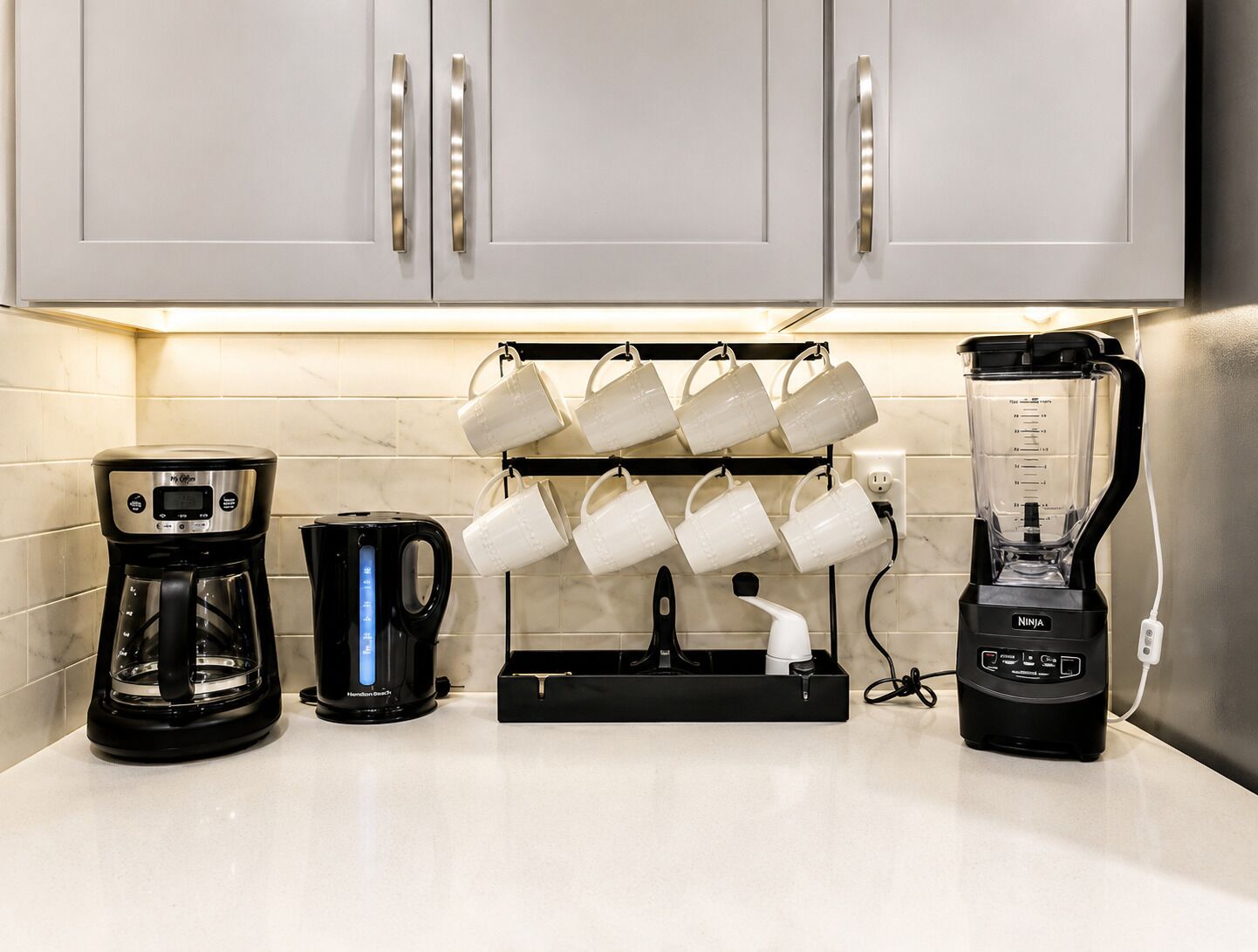 Een keuken met een koffiezetapparaat, een waterkoker, een muggenrek en een blender.