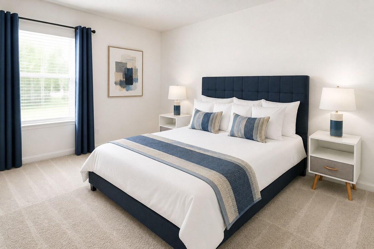 A bedroom with a bed, two bedside tables, a window with curtains, and a wall-mounted picture.