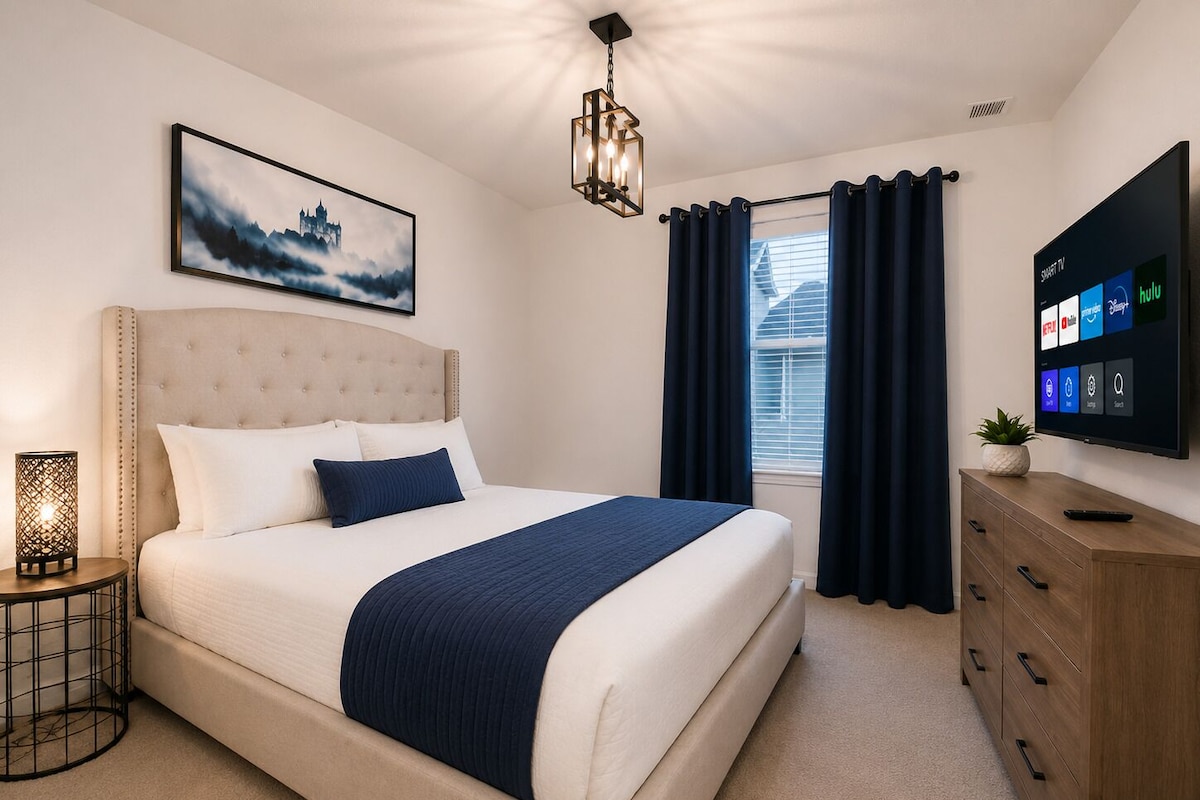 A bedroom with a bed, a bedside table with a lamp, a wall-mounted TV, and a window with curtains.