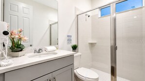 Un baño con lavamanos blanco, inodoro, ducha con puerta de cristal y espejo.