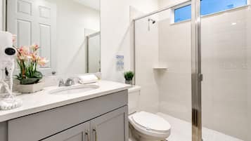 Een badkamer met een witte wastafel, toilet, douche met glazen deur en spiegel.