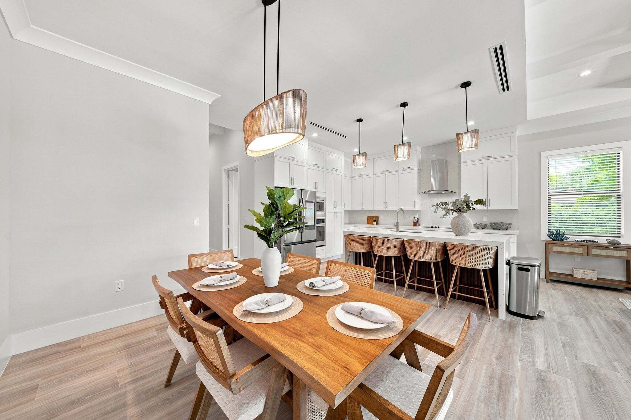 A modern kitchen with white cabinets, stainless steel appliances, and a wooden dining table set for four.