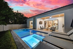 A modern house with a swimming pool, a patio with lounge chairs, and a view of the backyard. - New! Dream Chaser • New Luxury Build • Heated Saltwater Pool/Spa • 1 Mile to Vanderbilt Beach! (Naples)