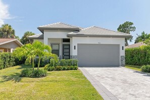 A modern two-story house with a garage, surrounded by well-maintained landscaping and a clear sky. - New! Dream Chaser • New Luxury Build • Heated Saltwater Pool/Spa • 1 Mile to Vanderbilt Beach! (Naples)