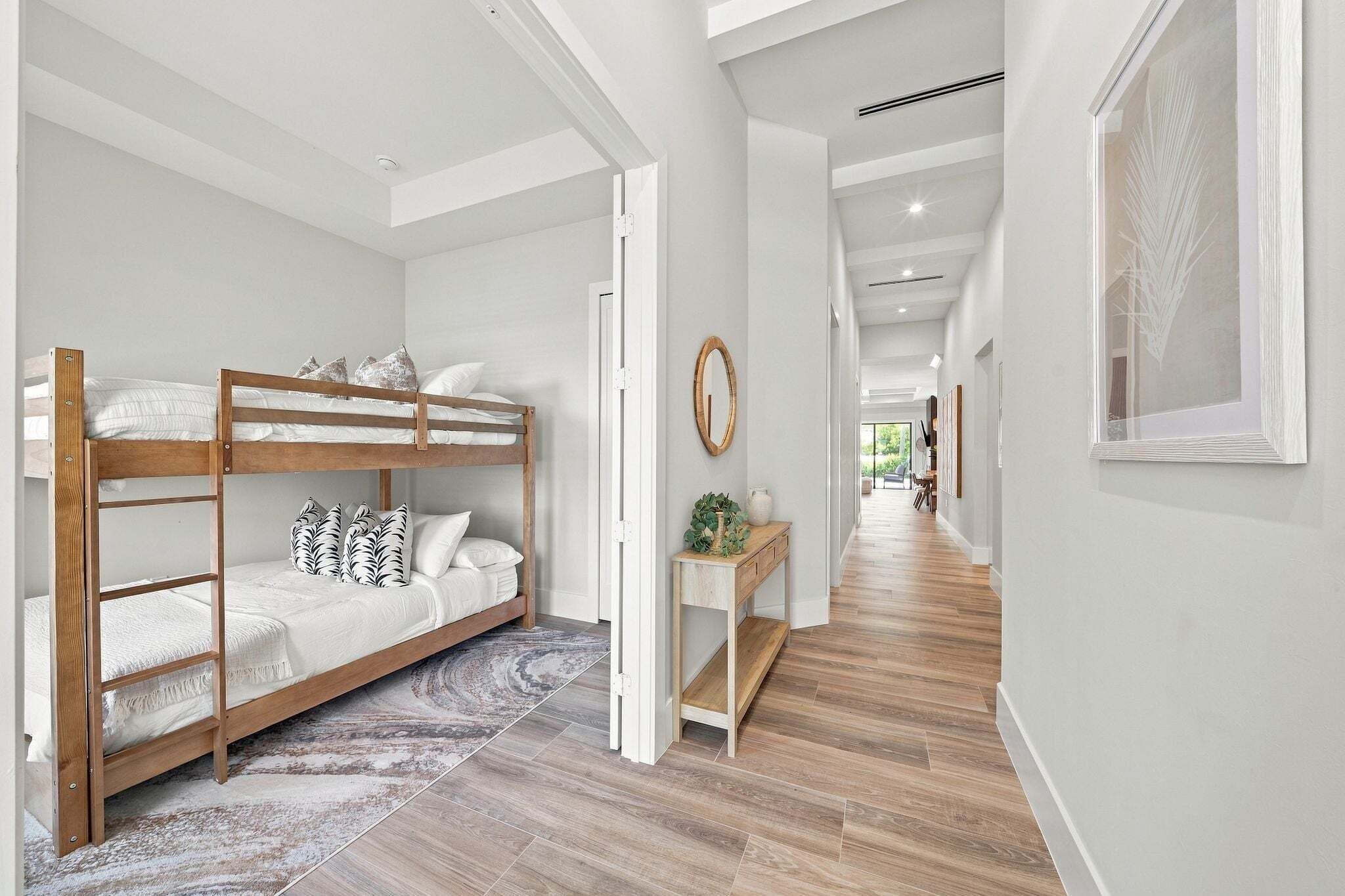 A modern interior with a bunk bed, a hallway with a wooden floor, and a view into another room.