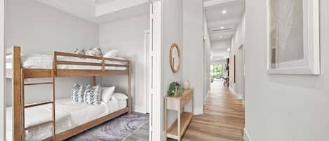 A modern interior with a bunk bed, a hallway with a wooden floor, and a view into another room.