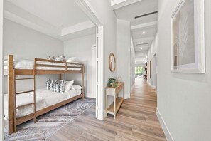 Un interior modern amb un llit superposat, un passadís amb terra de fusta i vista a una altra habitació.
