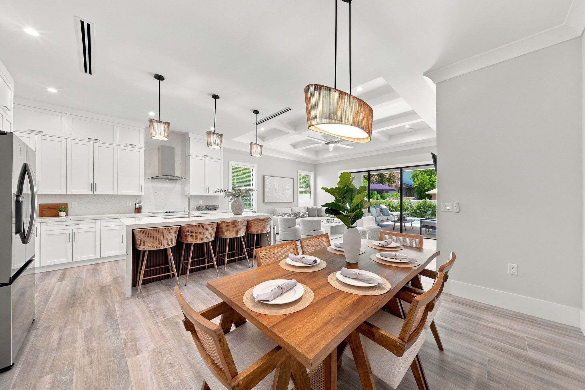 A modern kitchen with white cabinets, a wooden dining table set for four, and a large window overlooking a garden.