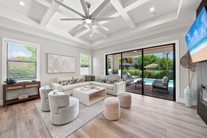 A modern living room with a sectional sofa, a coffee table, and a ceiling fan. - New! Dream Chaser • New Luxury Build • Heated Saltwater Pool/Spa • 1 Mile to Vanderbilt Beach! (Naples)
