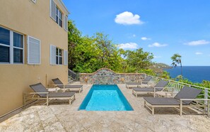 A pool area with lounge chairs, a stone wall, and a view of the ocean. - 3 King Suites | Pool + Mahogany Run | Magens Bay (St. Thomas)