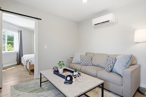 A modern living room with a sofa, a coffee table, and a potted plant. - Three Downtown Apartments | large groups | private | laundry (Traverse City)