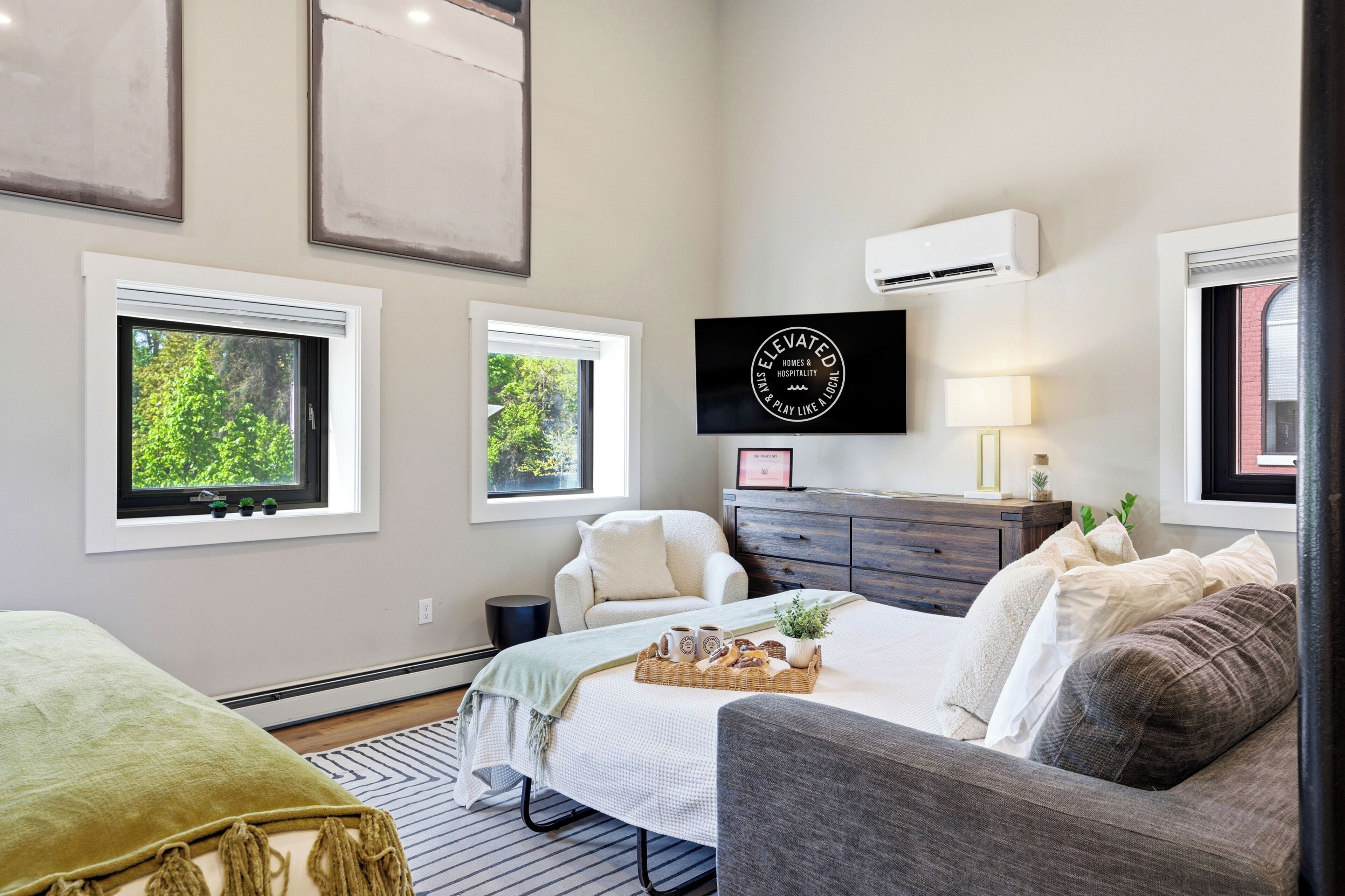 A bedroom with a bed, a chair, a dresser, and a wall-mounted air conditioner.