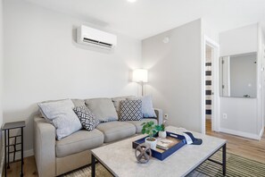 A modern living room with a sofa, coffee table, and a wall-mounted air conditioner. - Three Downtown Apartments | large groups | private | laundry (Traverse City)