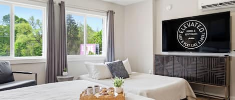 A hotel room with two beds, a TV, and a view of greenery outside.