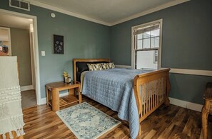 Een slaapkamer met een houten bed, een nachtkastje, een vloerkleed en een raam.