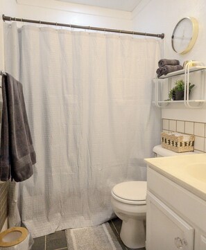 Een badkamer met douchegordijn, toilet, wastafel met spiegel en een handdoekrek met handdoeken.