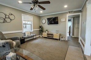 Een woonkamer met een plafondventilator, een flatscreen-televisie, een bank, een salontafel en een dressoir.