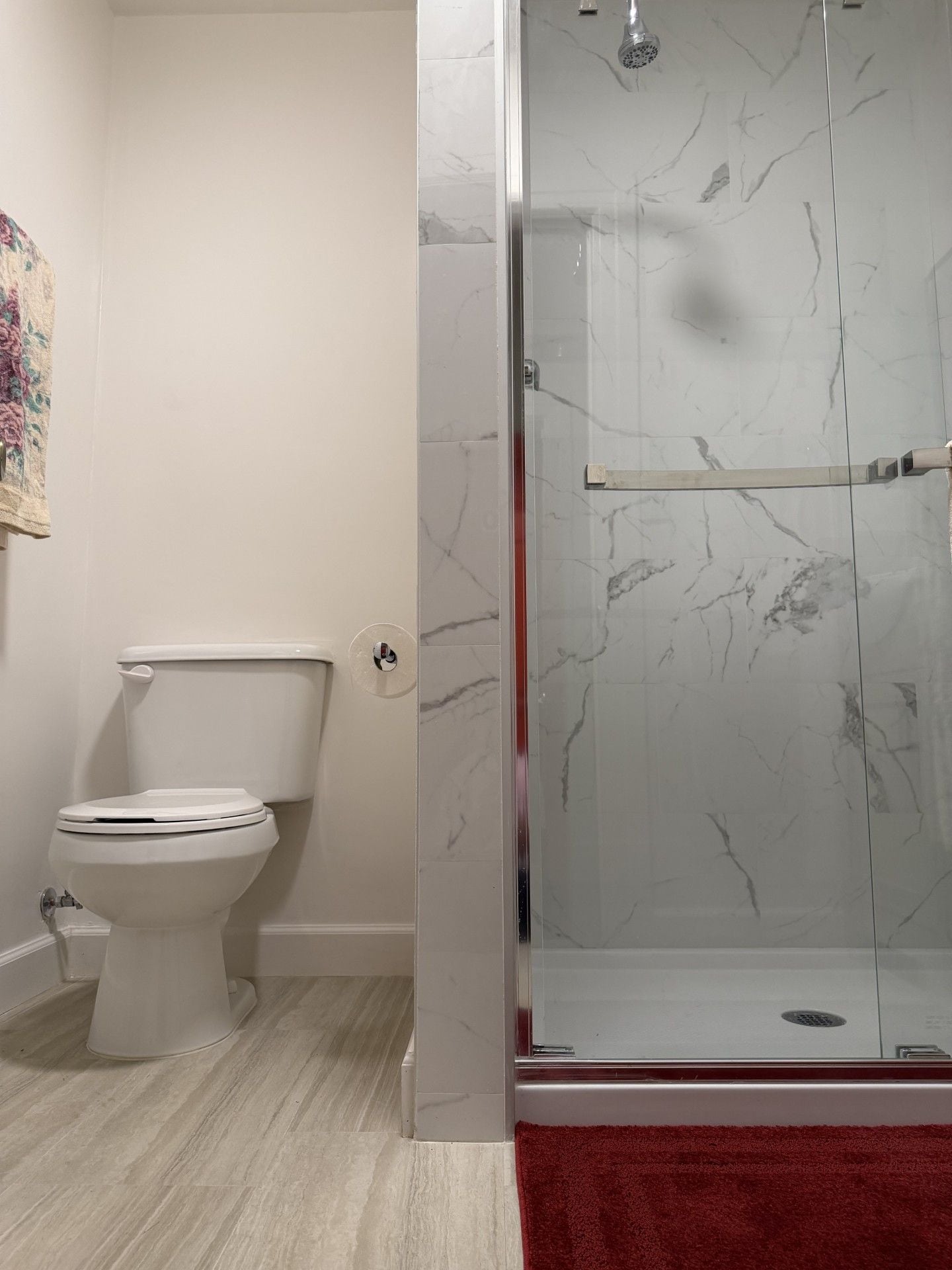 A bathroom with a toilet, a glass-enclosed shower, and a red bath mat.