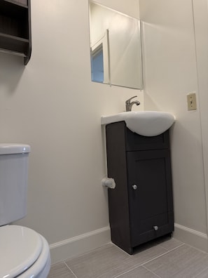 A bathroom with a toilet, a sink with a mirror above it, and a cabinet below.
