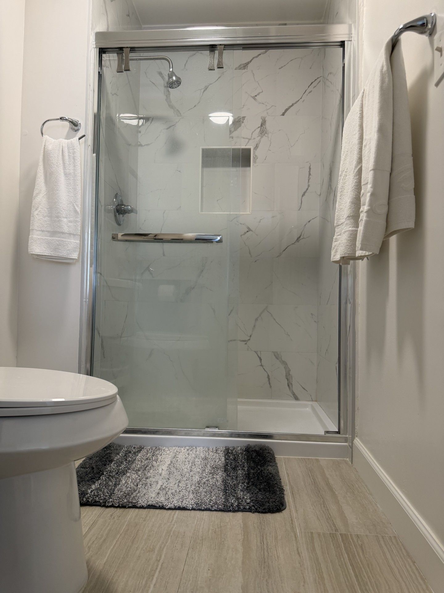 A bathroom with a glass shower enclosure, a toilet, and a rug.