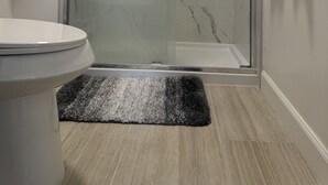 Un baño con cabina de ducha de vidrio, inodoro y alfombra.