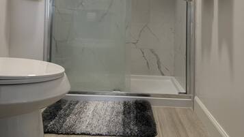 A bathroom with a glass shower enclosure, a toilet, and a rug.