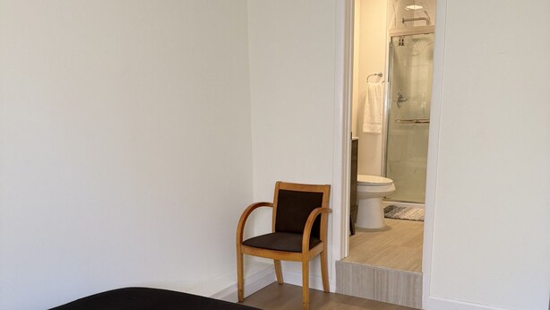 Un dormitorio con una cama, una silla y un baño visible a través de una puerta abierta.