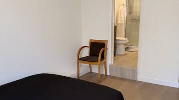 A bedroom with a bed, a chair, and a bathroom visible through an open door.