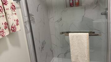 A glass-enclosed shower with a marble wall, a towel rack with a patterned towel, and a small shelf with toiletries.