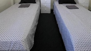Una camera matrimoniale con due letti singoli, ognuno con un cuscino e un comodino.