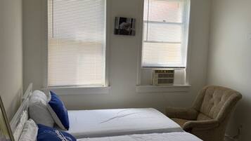 A bedroom with two beds, a chair, and a ceiling fan.