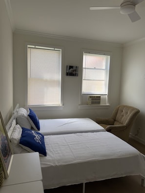 A bedroom with two beds, a chair, and a ceiling fan.