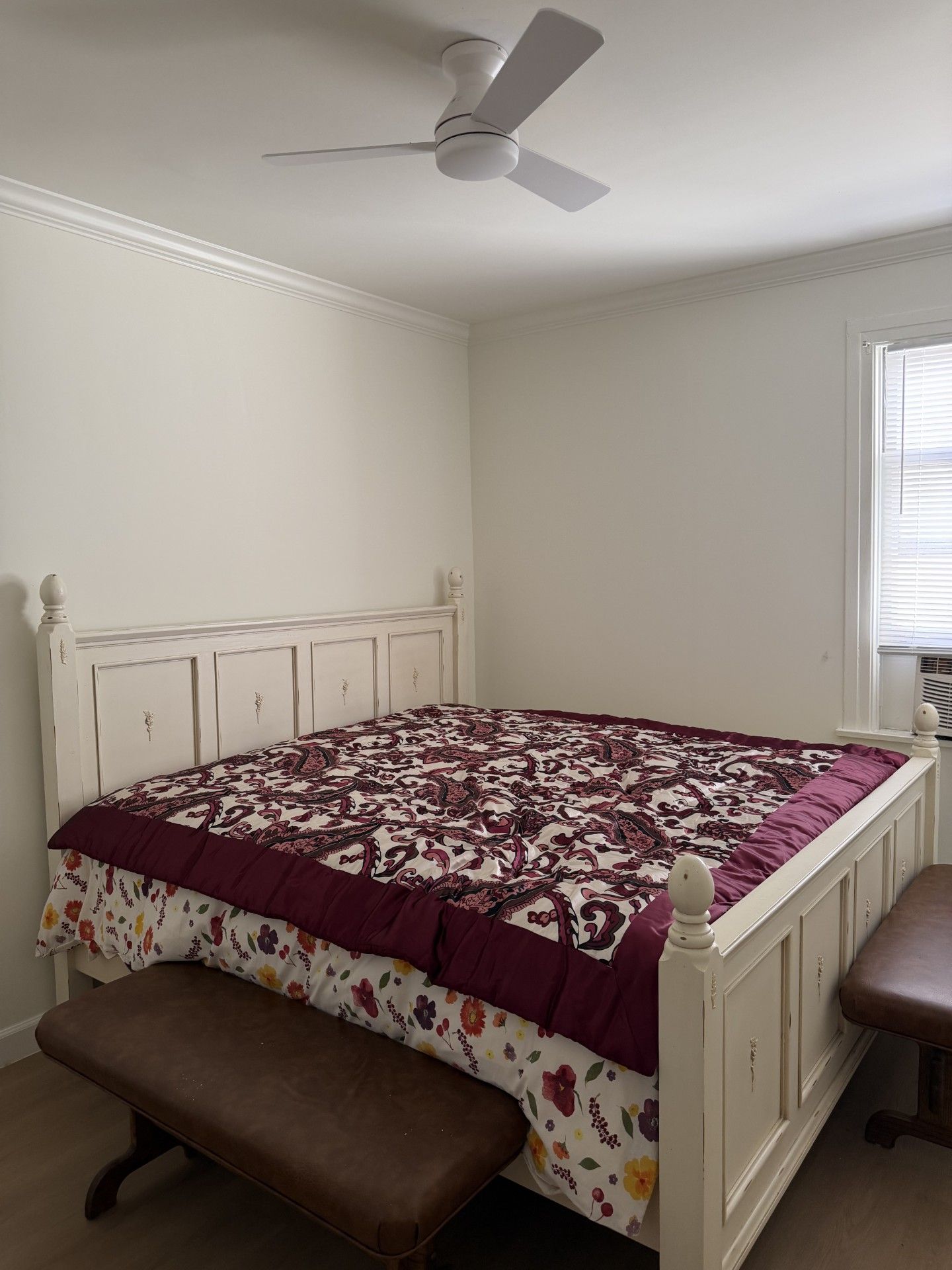 Un dormitorio con cama, banca, ventilador de techo y ventana.