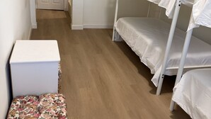Una habitación con una cama litera, un pequeño aparador blanco y un otoman con estampado floral.
