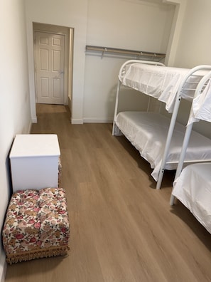 Una habitación con una cama litera, un pequeño aparador blanco y un otoman con estampado floral.