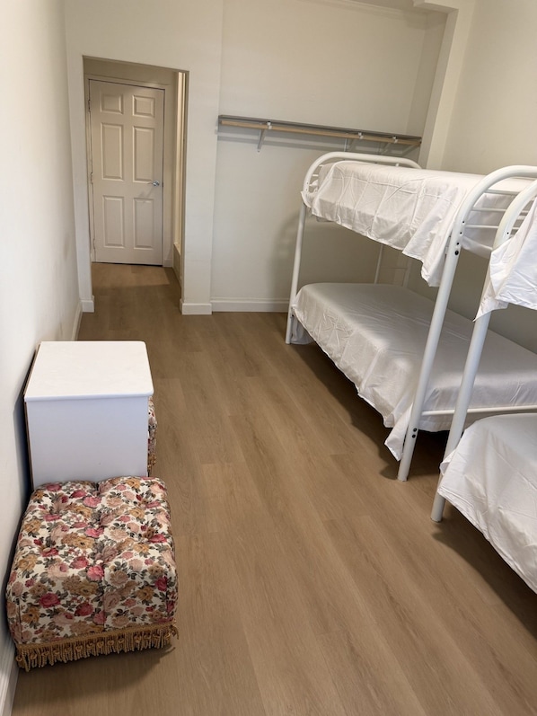 A room with a bunk bed, a small white chest of drawers, and a floral-patterned ottoman.
