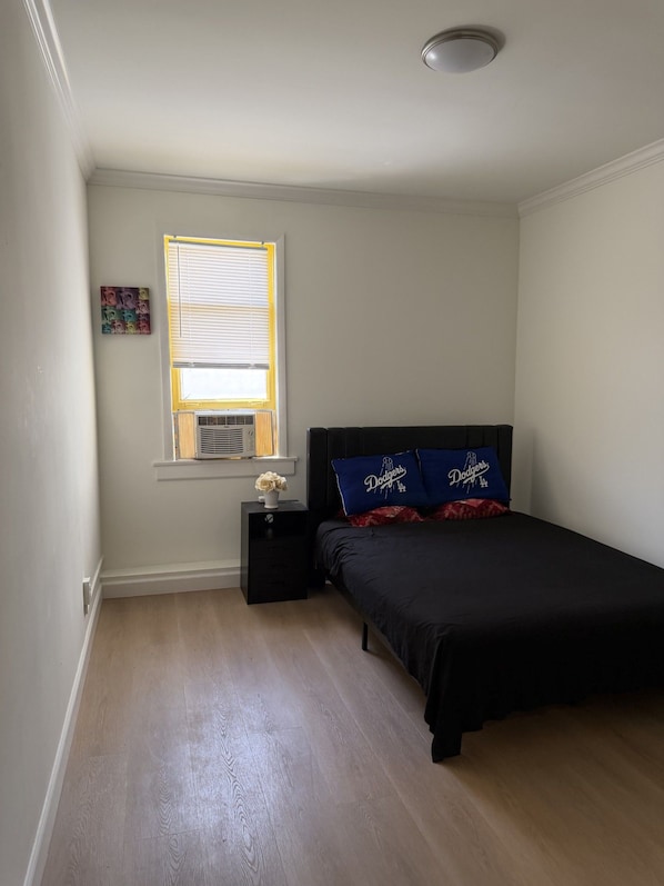 A bedroom with a bed, a nightstand, a window with blinds, and a small decorative item on the nightstand.