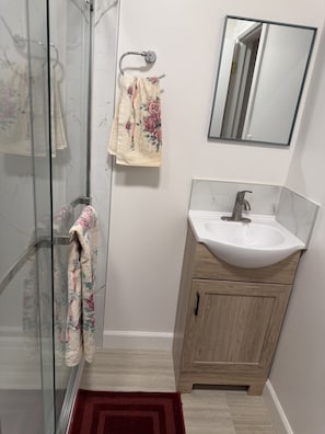 A bathroom with a glass shower enclosure, a wooden cabinet with a sink, and a mirror on the wall.