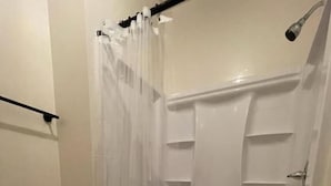 Una doccia con porta in vetro, tenda da doccia e ripiano integrato.