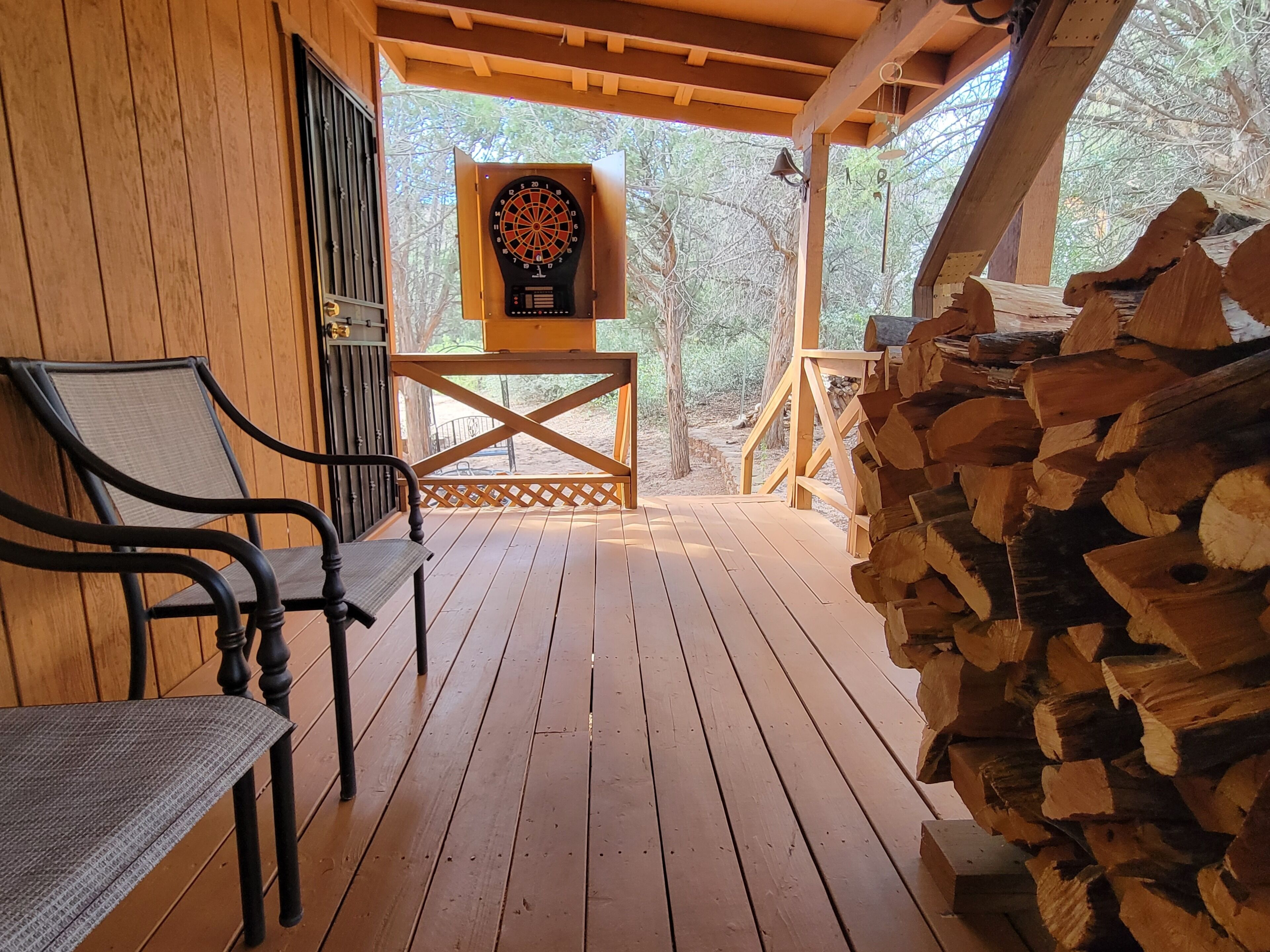 A wooden deck with a dartboard, a chair, and a stack of firewood.