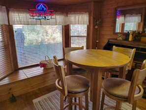 A wooden interior with a round table and chairs, a neon sign, and a window with blinds. - Cozy Cabin between the Pines (Payson)