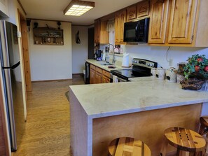 A kitchen with wooden cabinets, a stainless steel refrigerator, a microwave, and a central island with stools. - Cozy Cabin between the Pines (Payson)