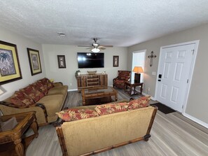 Una sala de estar con sofá, sillón, mesa de centro y televisor.